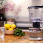 Impression: Lotus NATURA PLUS Glas-Filterkanne Anthrazit auf Holztisch mit Wasserglas