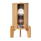 Ein Glas-Wasserfilter mit Bambusgehäuse und sichtbaren Filterstufen steht auf einem Bambussockel.